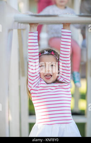 Girl at preschool, portrait hanging from climbing frame in garden Stock Photo
