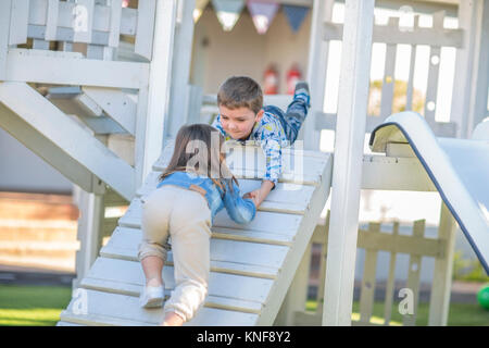 Girl and boy at preschool, helping hand to crawl up ramp on climbing frame in garden Stock Photo