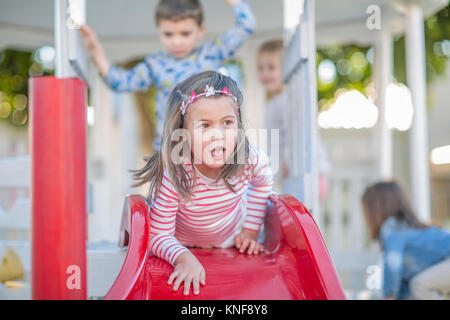 Girl at preschool, lying at top of playground slide in garden Stock Photo