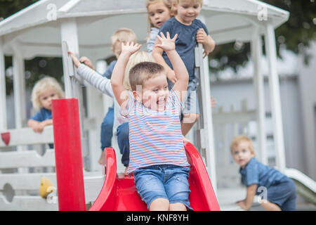 Boys and girls at preschool, sliding on playground slide in garden Stock Photo