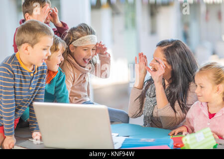 Mid adult woman, sitting with young children, looking at laptop Stock Photo