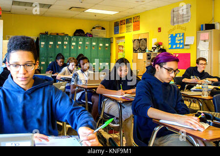 Teenage boys and girls doing schoolwork on laptops at classroom desks ...