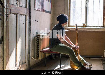 Young man sitting on chair, holding guitar Stock Photo