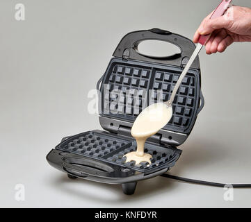 Hand with big spoon Pouring fresh pastry into waffle maker Stock Photo