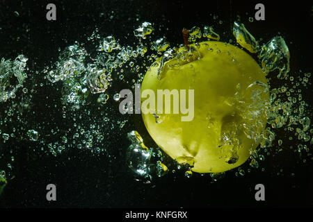 A green apple in a stream of water and air on the black background Stock Photo