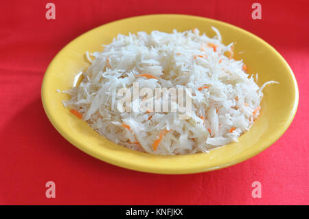 Sauerkraut with carrots in a yellow plate on the red background. Stock Photo