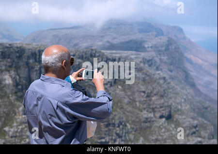 Tourist using a mobile phone to take a photograph of the view from the top of Table Mountain in Cape Town, South Africa Stock Photo