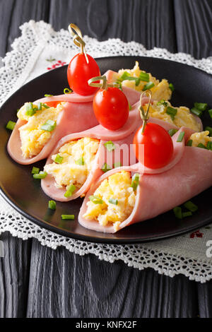 Festive snack: roll ham stuffed with scrambled eggs and tomatoes close-up on a plate. Vertical Stock Photo