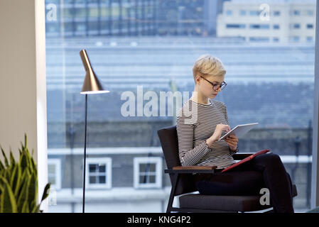Caucasian businesswoman in a contemporary office tapping the screen of a mobile device Stock Photo