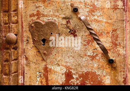 Heart-shaped keyhole and twisted metal handle on a peeling woodwormy wooden door in Sarlat, France Stock Photo