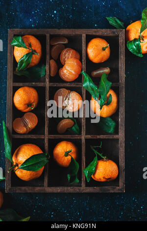 Tangerines in a wooden case on a dark background. An assortment of clementines with green leaves. Dark food photography with vibrant orange fruit and  Stock Photo