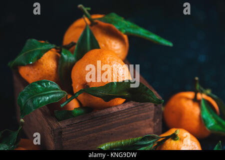 Tangerines in a wooden box on a dark wooden background. Vibrant ripe fruit concept. Dark food photography. Stock Photo