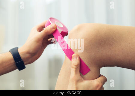 sport injury - physical therapist placing pink kinesio tape on patient knee Stock Photo