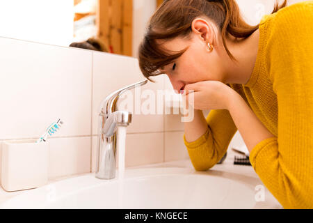 Young vomiting woman near sink in bathroom Stock Photo