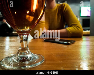 woman sitting at bar counter, glass of beer in from in focus Stock Photo