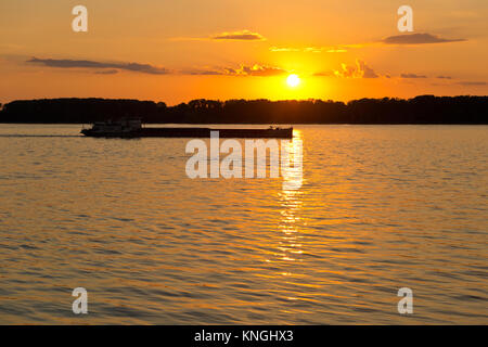 barge passes through the channel of the river Volga, breaking the light beam reflected on the water of the setting sun. Samara, Samara Oblast, Russia, Stock Photo