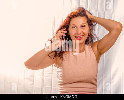before and after skin retouching in middle aged attractive woman smiling and holding her head while phoning Stock Photo