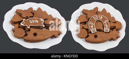 Two white plates with Christmas and New Year gingerbreads. Piggy and horseshoe for good luck with 2018 inscriptions. Isolated on dark gray background. Stock Photo