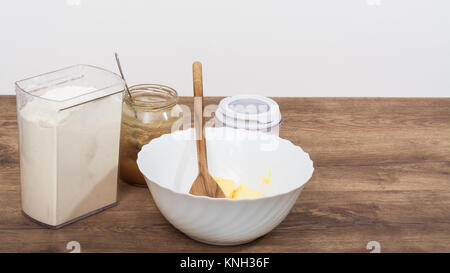 Ingredients for making sweet dough on the kitchen table. Flour, honey, sugar and butter in white bowl on the beautiful wooden background. Stock Photo