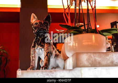 A small, ceramic painted boxer dog figurine on the counter of a colorful bar with red mood lighting in Rouen France. Stock Photo