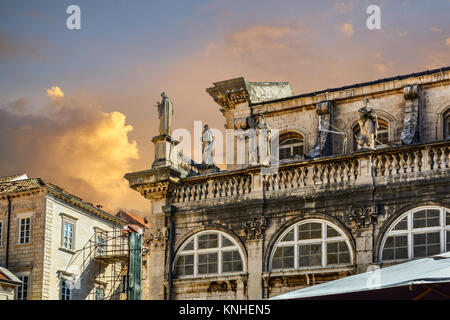 Ancient statues line an old building in the walled city center of Dubrovnik Croatia in the late afternoon, colorful sky Stock Photo