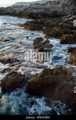 Waves break over rocks on the coast Kardimyli, west coast of Greece, at sunset Stock Photo