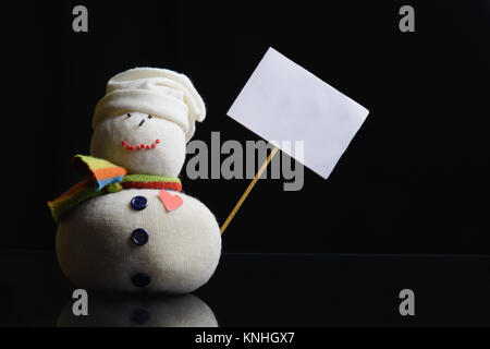 Snowman figure on a black background holding an empty placard board with stick attached. A contrasty low key photograph. Stock Photo