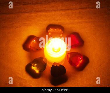 Burning candle lying around it is transparent with colored stones in the form of hearts. Still life Stock Photo