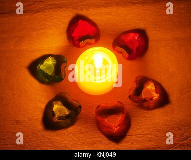 Burning candle lying around it is transparent with colored stones in the form of hearts. Still life Stock Photo