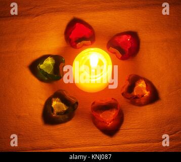 Burning candle lying around it is transparent with colored stones in the form of hearts. Still life Stock Photo