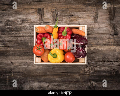 Fresh tasty red and yellow vegetables in wooden crates on a rustic wooden table Stock Photo