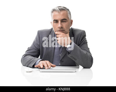 Pensive businessman sitting at office desk and working with a computer, he is thinking with hand on chin Stock Photo
