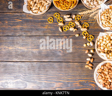 Top view of various beer snacks in plates like pistachios, small pretzels and different peanuts on dark wooden desk. Food and beverages concept Stock Photo
