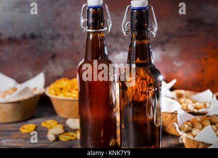Two beer bottles, plates with pistachios, small pretzels and peanuts on background. Food and beverages concept Stock Photo