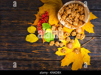 Top view of slightly scattered walnuts lying on leaves near wooden plate with walnuts and rowan on wooden desk. Mockup for seasonal offers and holiday Stock Photo