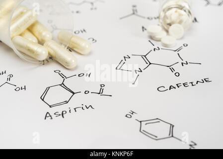 Aspirin in capsules and caffein in tablets on paper with their chemical formula Stock Photo