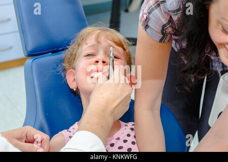 Preschooler child is at dentist office, medical forceps with just extracted milk tooth. Stock Photo