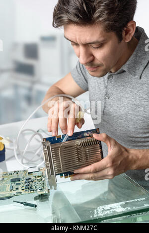 Young male tech cleans faulty computer processor in hardware repair workshop. Focus on the face and fingers Stock Photo