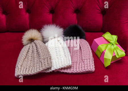 winter knitted hats with a fur ball lay on the red couch. knitted hats and a New Year's gift Stock Photo