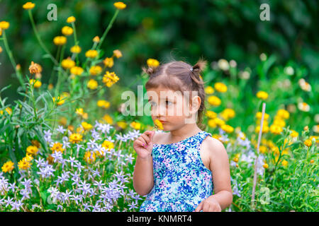 your girl with brown hair smelling a yellow flower in a pretty flower garden Stock Photo