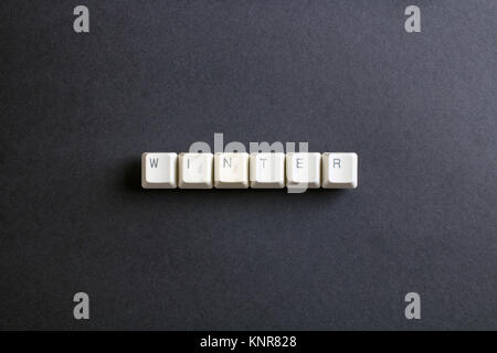 Winter word is written with computer keys button. Flat lay view from above on the table with computer keyboard keys buttons on a dark background. Stock Photo
