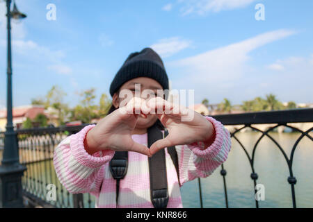 Asian little girl showing hand make heart shape with happiness in vacation travel, select focus on hands shallow depth of field Stock Photo