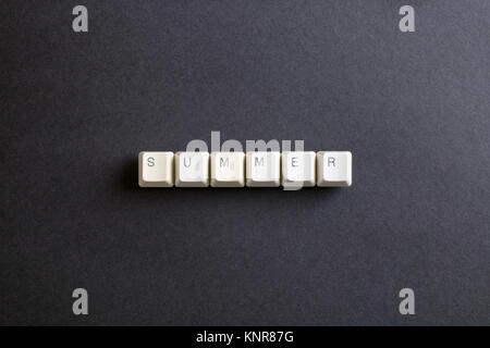 Summer word is written with computer keys button. Flat lay view from above on the table with computer keyboard keys buttons on a dark background. Stock Photo