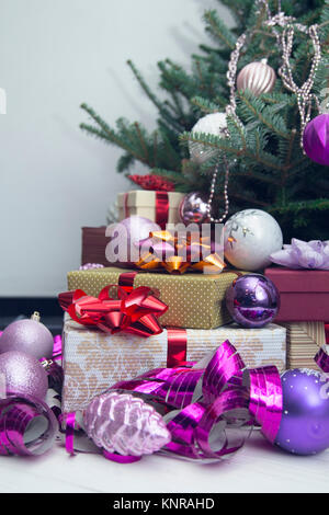 New Year's decor idea for a living room with gifts under a Christmas tree. A pile of gift boxes with bright ribbons and shiny purple Christmas-tree or Stock Photo