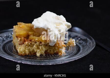 Sponge apple cake with whipped cream on glass plate and solid black background Stock Photo