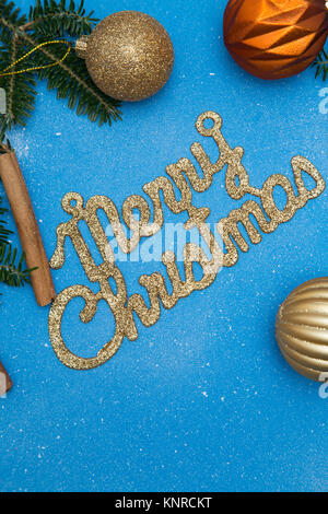 A gold gleaming Merry Christmas inscription with spruce branches and gold balls made of glass on a blue background