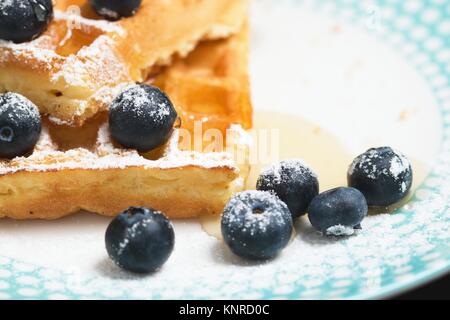 Detail of several blueberries iced with powdered sugar in puddle of honey on a plate next to waffles. Stock Photo