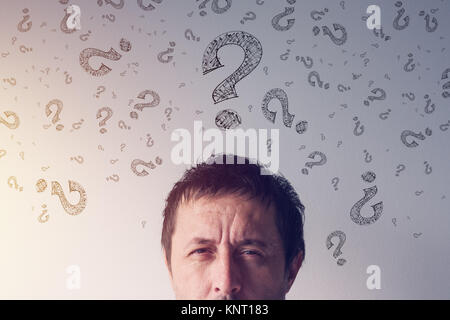 Question mark, looking for answers. Perplexed man with scribbled interrogation point symbols around his head. Stock Photo