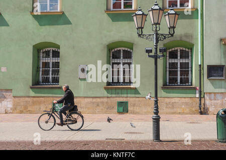 Stare Miasto Krakow, a cyclist rides past the colourful facade of a building in Little Market Square (Maly Rynek) in Krakow old town (Stare Miasto). Stock Photo