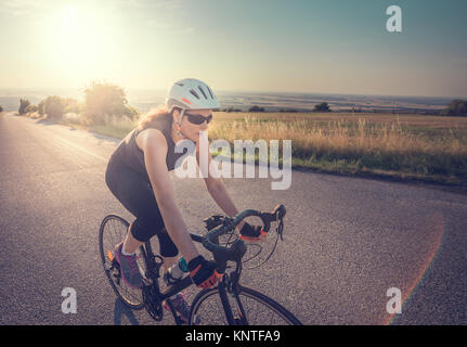 Pretty Young Fit Woman Riding Bike Up the Hill at Sunset Stock Photo